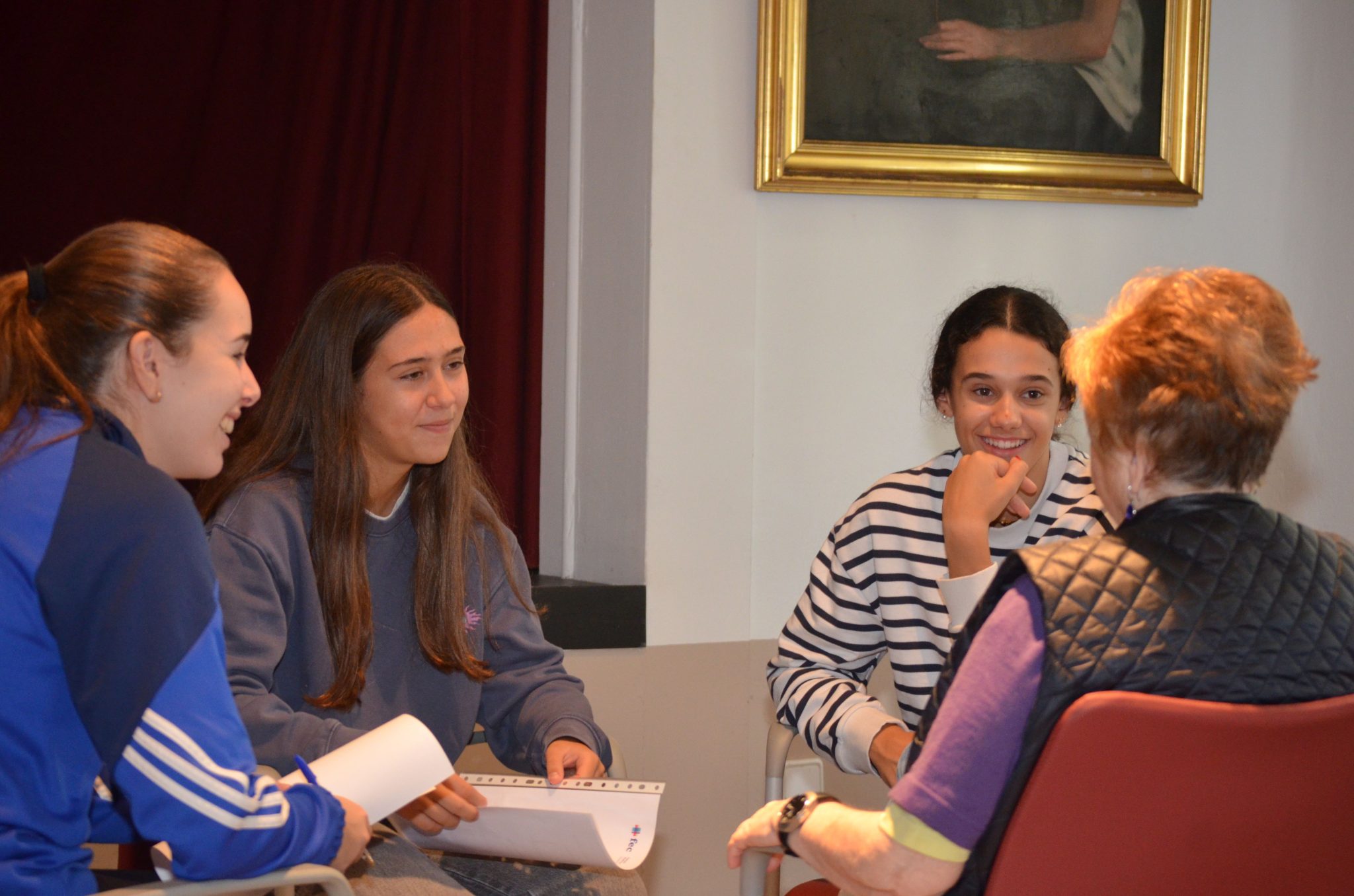 Alumnas de primero de bachiller del Colegio FEC vedruna charlan con una persona residente de la Casa de Misericordia que se encuentra de espaldas.